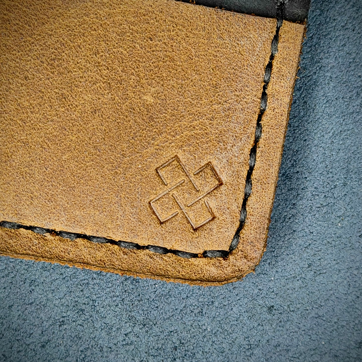 Back view close-up of the design logo emboss on the back of The Houdini card holder – focusing on the fine grain detail of ethically sourced black and sandstorm brown full-grain leather and meticulous saddle stitching. Showcases the subtle artistry and understated luxury of Novelty Atelier’s craftsmanship.