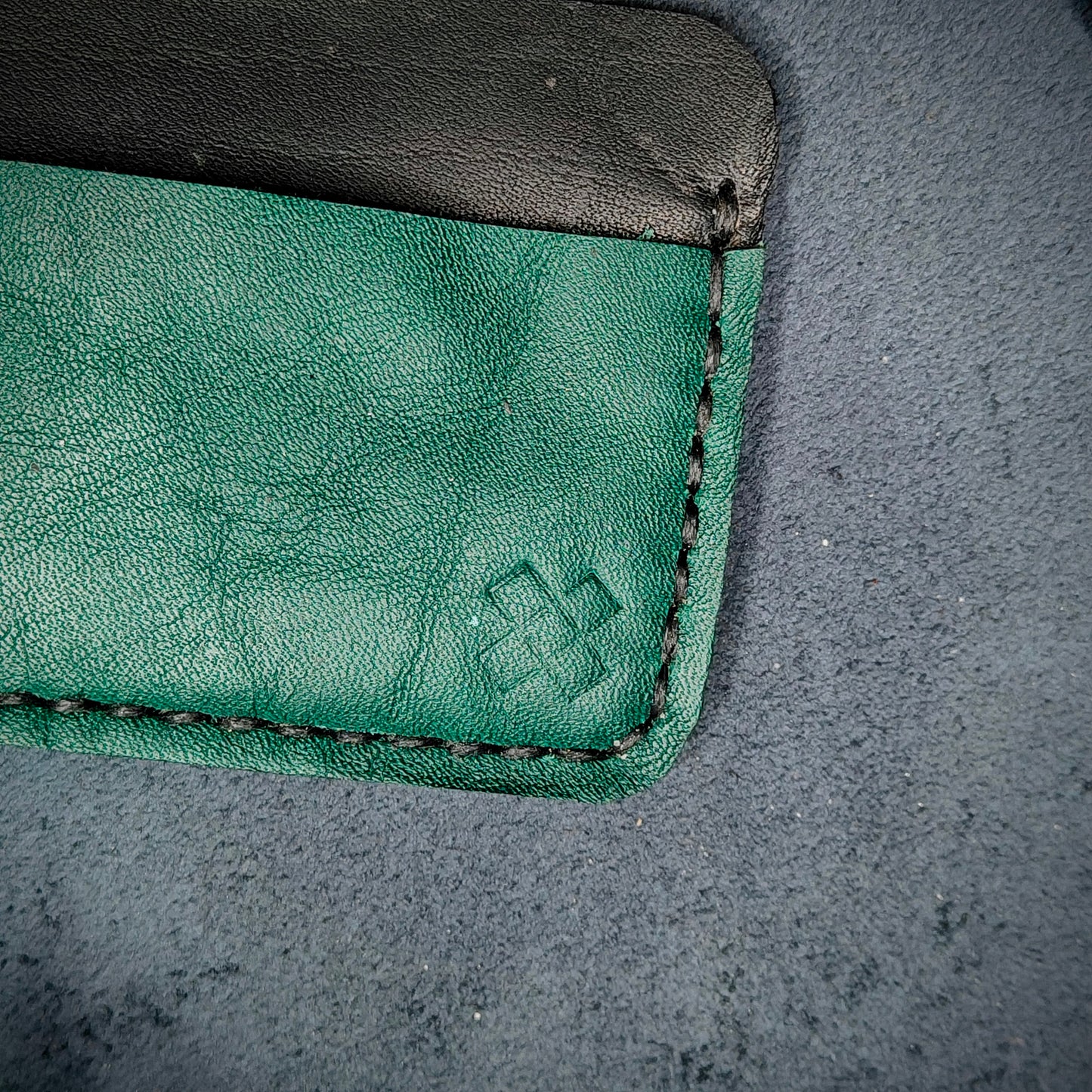 Back view close-up of the design logo emboss on the back of The Houdini card holder– focusing on the fine grain detail of ethically sourced green full-grain leather and meticulous saddle stitching. Showcases the subtle artistry and understated luxury of Novelty Atelier’s craftsmanship.
