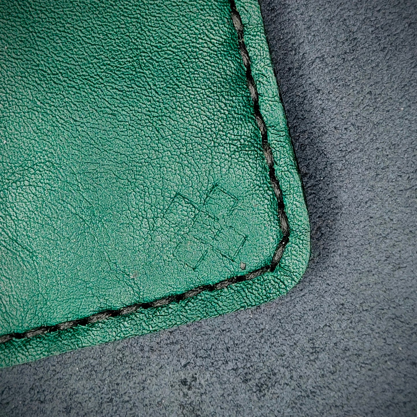 Back view close-up of the design logo emboss on the back of The Houdini card holder– focusing on the fine grain detail of ethically sourced green full-grain leather and meticulous saddle stitching. Showcases the subtle artistry and understated luxury of Novelty Atelier’s craftsmanship.