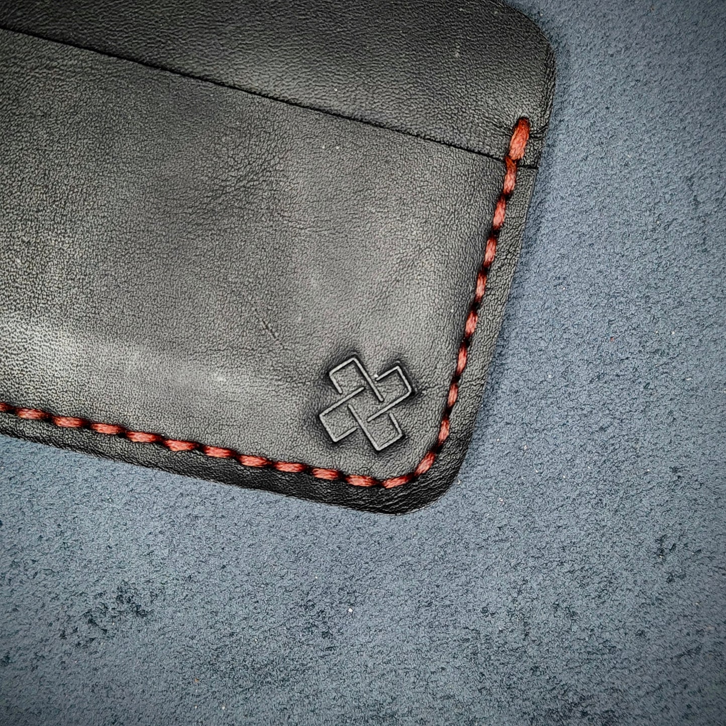 Back view close-up of the design logo emboss on the back of The Houdini card holder in horizontal configuration– focusing on the fine grain detail of ethically sourced black full-grain leather and meticulous red saddle stitching. Showcases the subtle artistry and understated luxury of Novelty Atelier’s craftsmanship.
