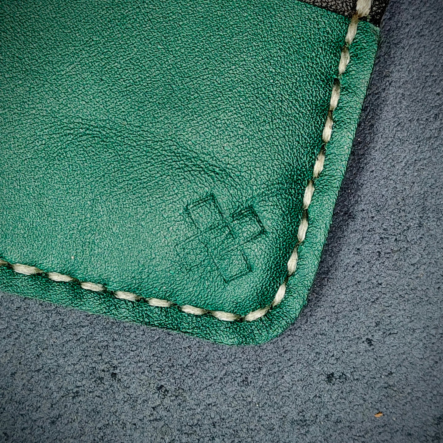 Back view close-up of the design logo emboss on the back of The Houdini card holder in horizontal configuration – focusing on the fine grain detail of ethically sourced green full-grain leather and meticulous saddle stitching. Showcases the subtle artistry and understated luxury of Novelty Atelier’s craftsmanship.
