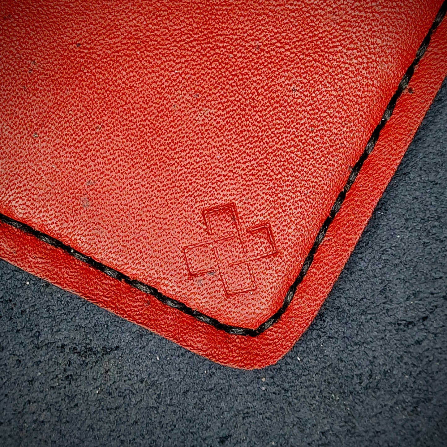 Back view close-up of the design logo emboss on the back of The Houdini card holder in vertical configuration– focusing on the fine grain detail of ethically sourced Red full-grain leather and meticulous black saddle stitching. Showcases the subtle artistry and understated luxury of Novelty Atelier’s craftsmanship.