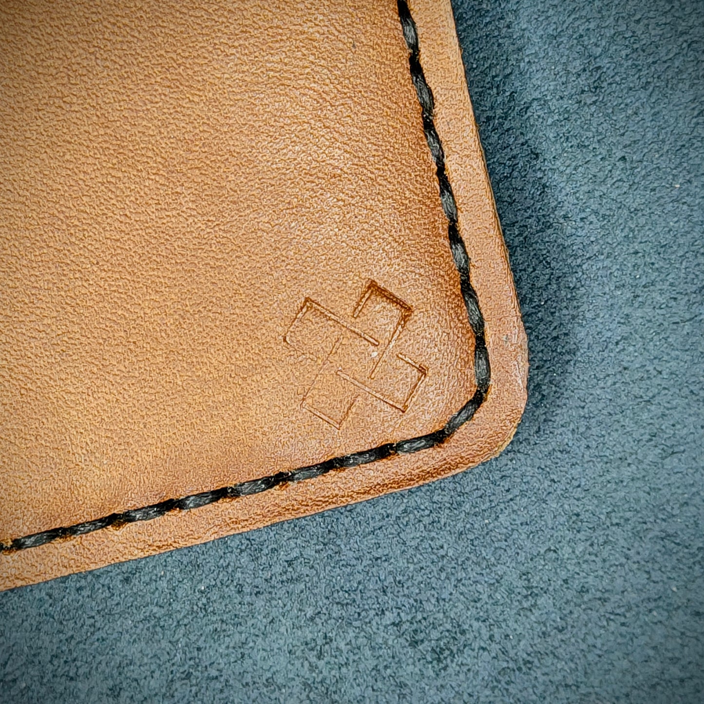 Back view close-up of the design logo emboss on the back of The Houdini card holder in vertical configuration– focusing on the fine grain detail of ethically sourced Tann full-grain leather and meticulous black saddle stitching. Showcases the subtle artistry and understated luxury of Novelty Atelier’s craftsmanship.