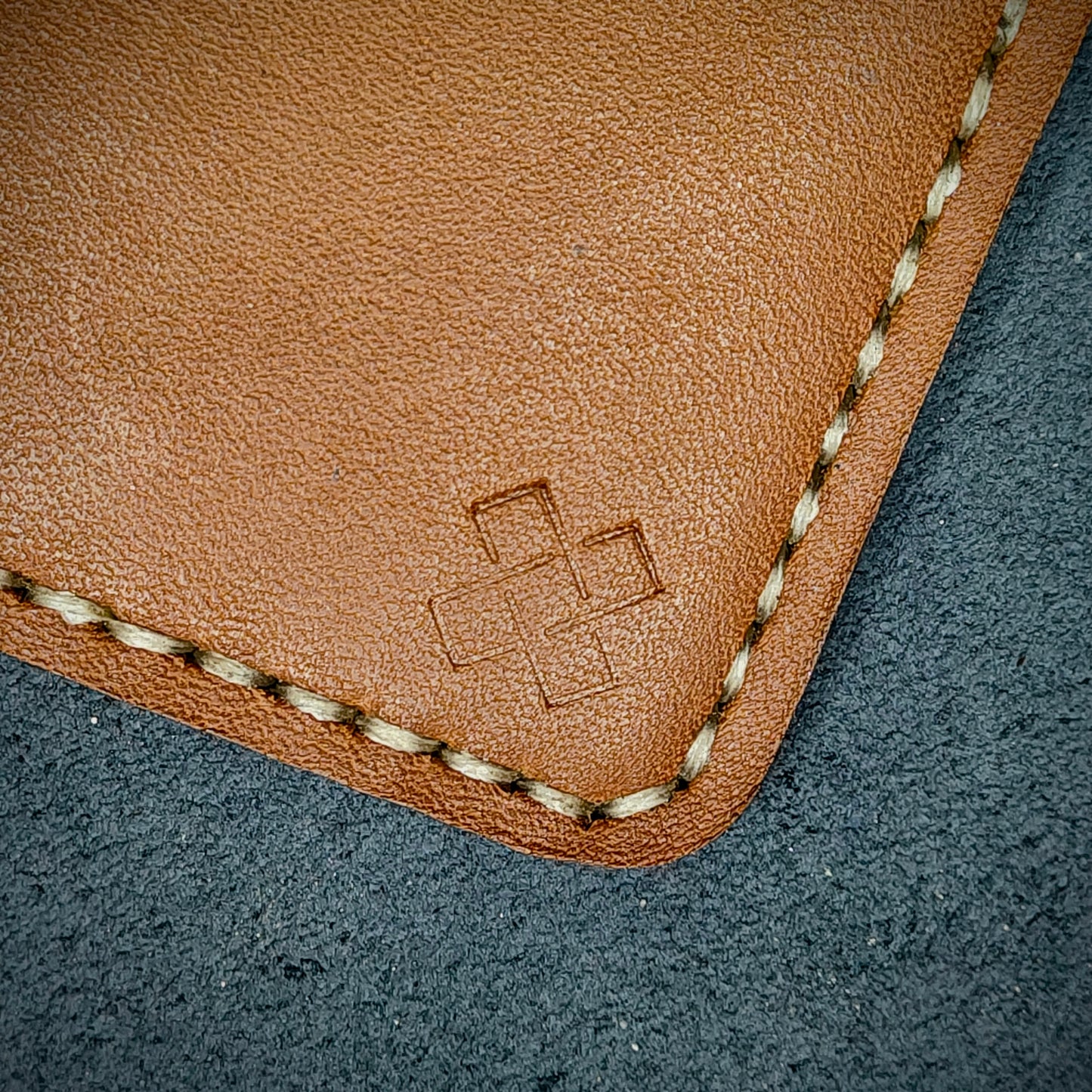 Back view close-up of the design logo emboss on the back of The Houdini card holder in vertical configuration – focusing on the fine grain detail of ethically sourced Tann full-grain leather and meticulous off-white saddle stitching. Showcases the subtle artistry and understated luxury of Novelty Atelier’s craftsmanship.