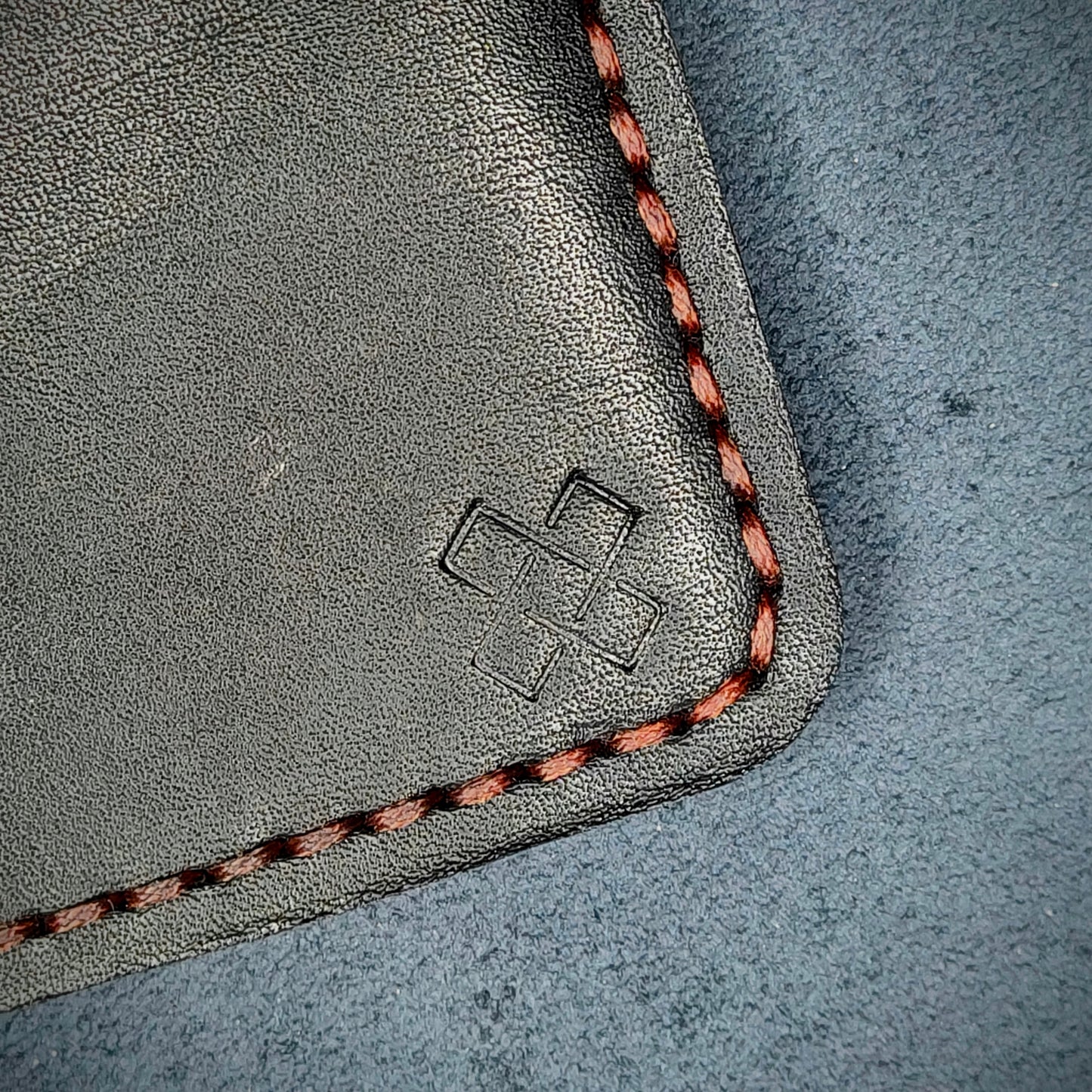 Back view close-up of the design logo emboss on the back of The Houdini card holder in vertical configuration– focusing on the fine grain detail of ethically sourced black full-grain leather and meticulous red saddle stitching. Showcases the subtle artistry and understated luxury of Novelty Atelier’s craftsmanship.