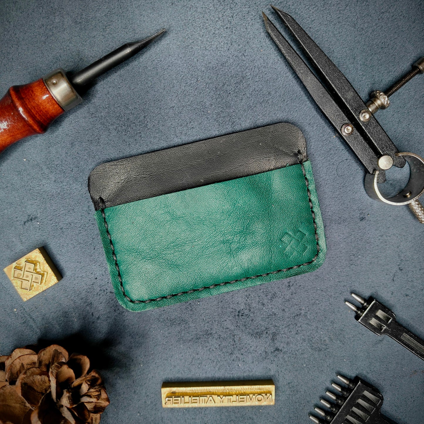 Back view of The Houdini minimalist leather card holder in horizontal configuration by Novelty Atelier – features a clean, functional layout with the design logo subtly stamped into green full-grain leather. Accented with black saddle stitching for a timeless aesthetic.