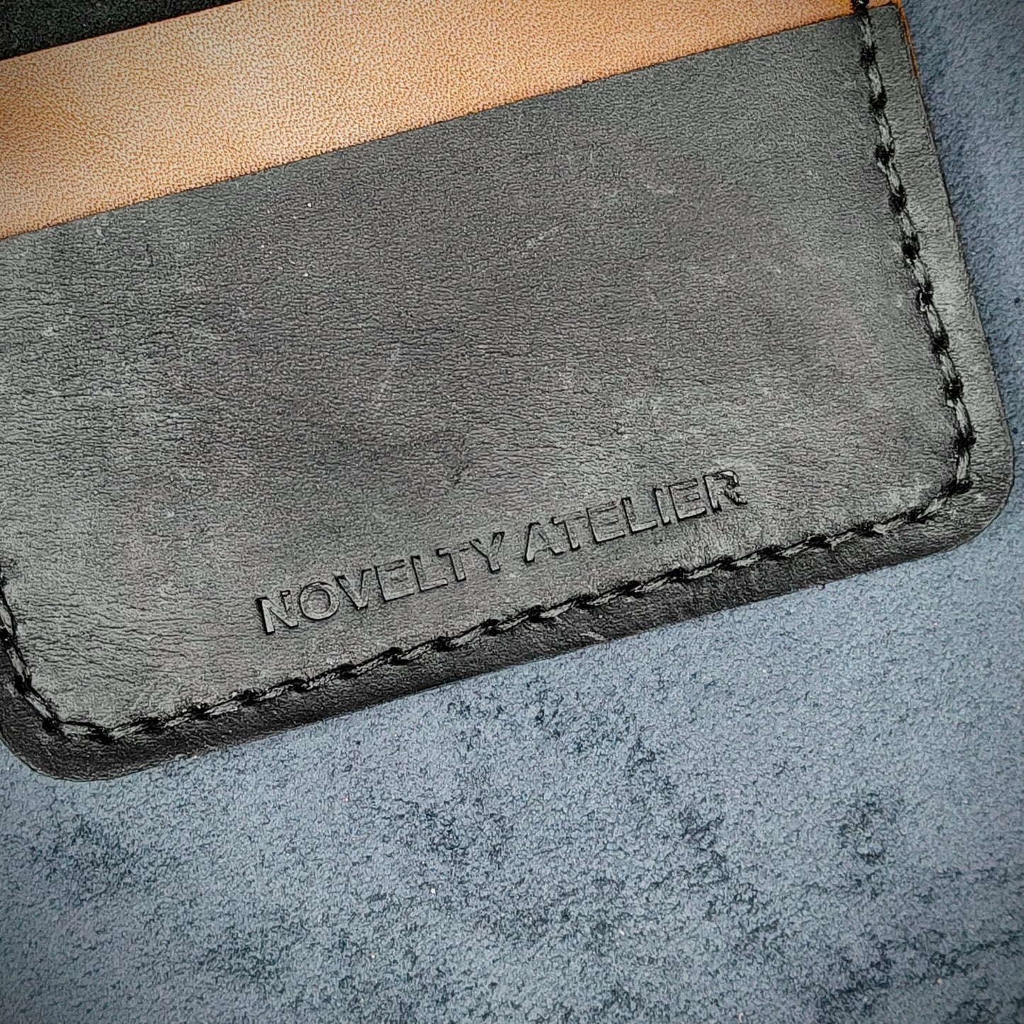 Close up of The Copperfield bifold card holder by Novelty Atelier detailed view of brand name logo embossed into Black and Brown full grain leather. Features precise saddle stitching in black thread and hand finished edges. Symbol of artisanal craftsmanship and functional luxury.