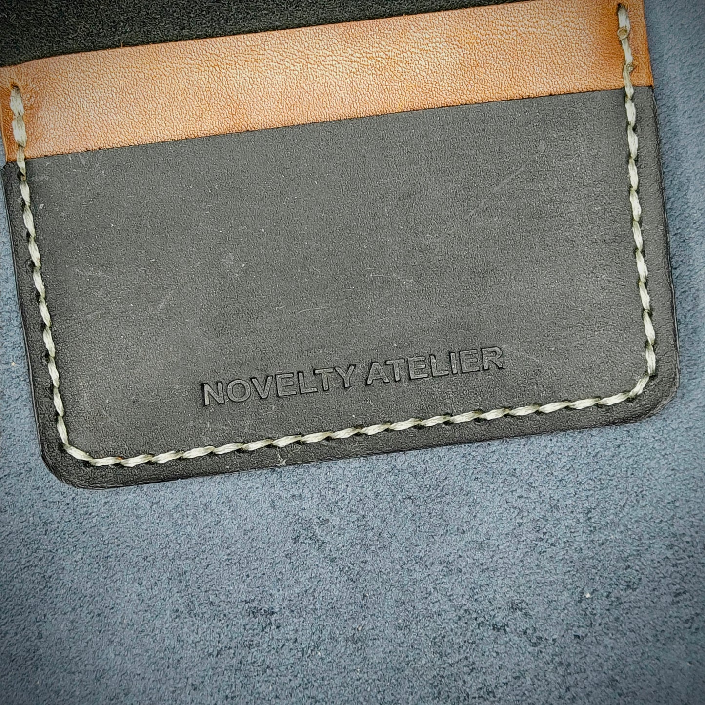 Close up of The Copperfield bifold card holder by Novelty Atelier detailed view of brand name logo embossed into Black and Brown full grain leather. Features precise saddle stitching in off white thread and hand finished edges. Symbol of artisanal craftsmanship and functional luxury.