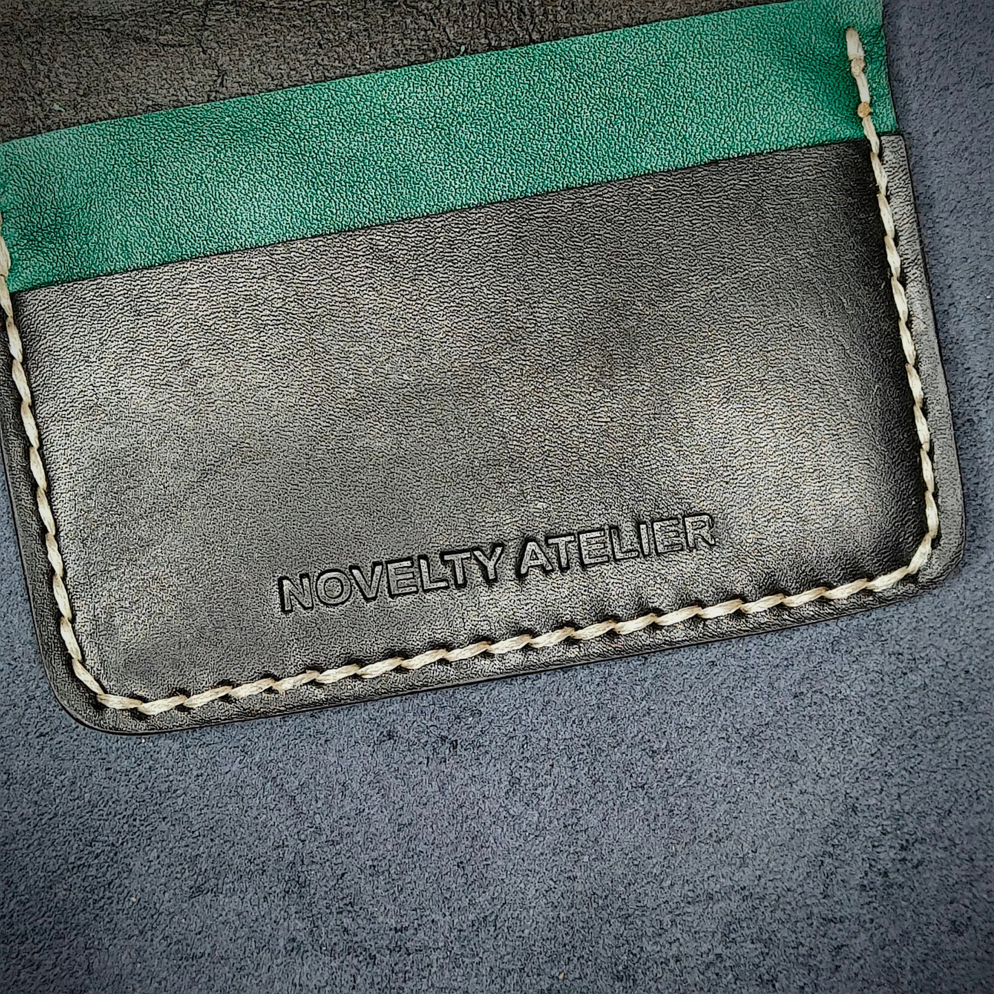 Close up of The Copperfield bifold card holder by Novelty Atelier detailed view of brand name logo embossed into Black and Green full grain leather. Features precise saddle stitching in off white thread and hand finished edges. Symbol of artisanal craftsmanship and functional luxury.