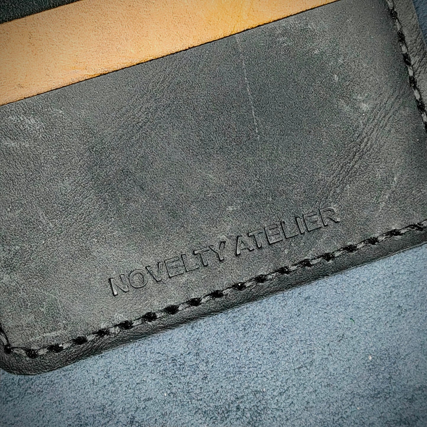 Close up of The Copperfield bifold card holder by Novelty Atelier detailed view of brand name logo embossed into Black and Mustard yellow full grain leather. Features precise saddle stitching in black thread and hand finished edges. Symbol of artisanal craftsmanship and functional luxury.