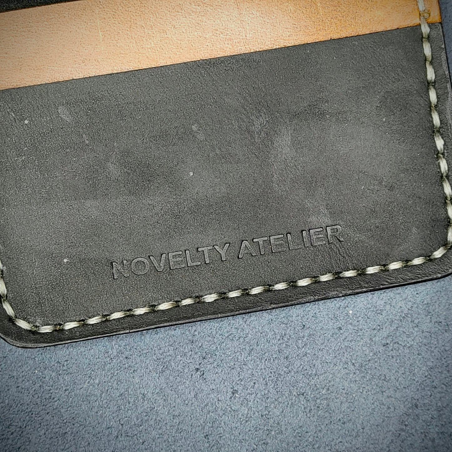 Close up of The Copperfield bifold card holder by Novelty Atelier detailed view of brand name logo embossed into Black and Mustard yellow full grain leather. Features precise saddle stitching in off white thread and hand finished edges. Symbol of artisanal craftsmanship and functional luxury.