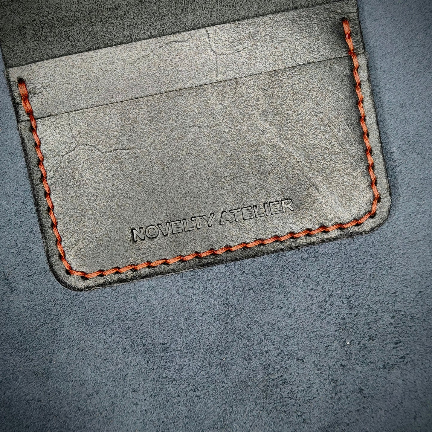 Close up of The Copperfield bifold card holder by Novelty Atelier detailed view of brand name logo embossed into Black full grain leather. Features precise saddle stitching in Red thread and hand finished edges. Symbol of artisanal craftsmanship and functional luxury.