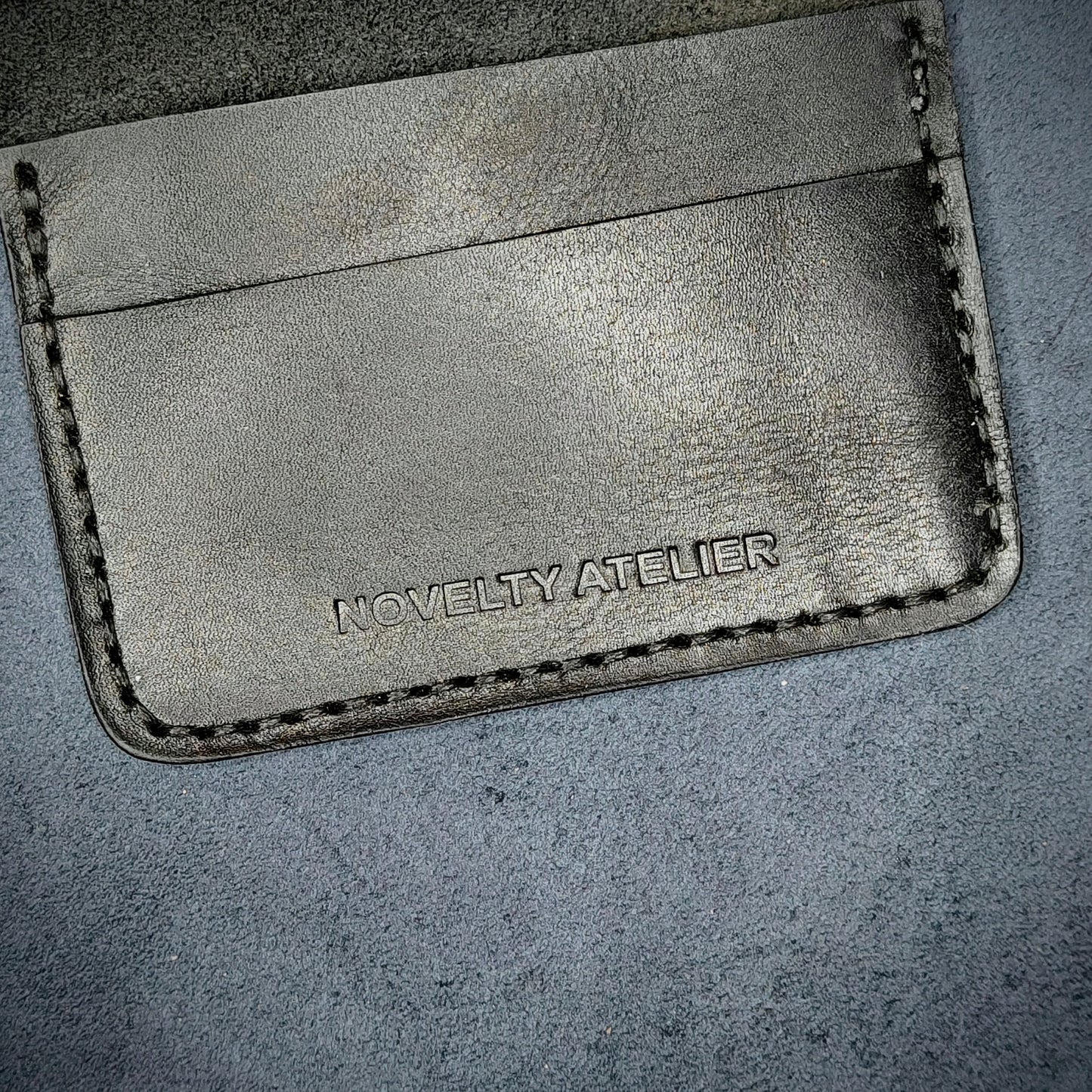 Close up of The Copperfield bifold card holder by Novelty Atelier detailed view of brand name logo embossed into Black full grain leather. Features precise saddle stitching in black thread and hand finished edges. Symbol of artisanal craftsmanship and functional luxury.