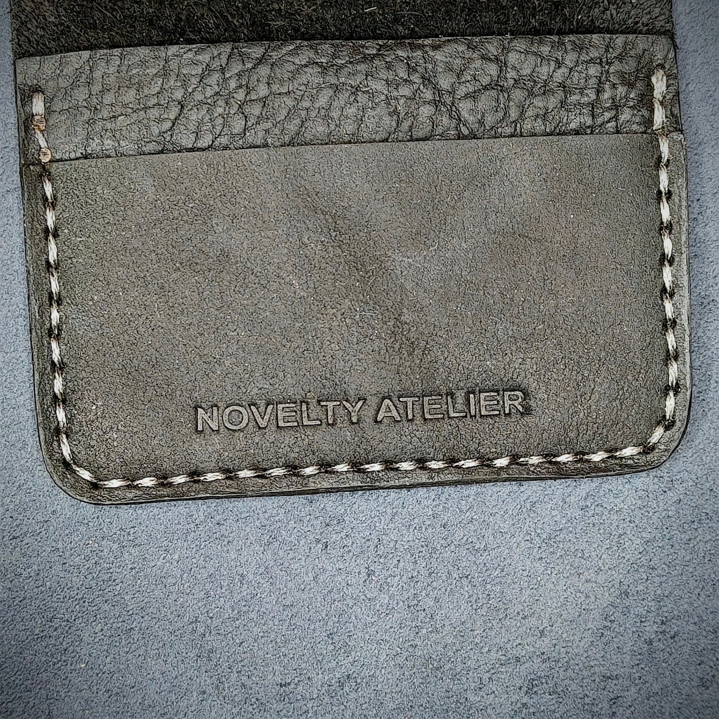 Close up of The Copperfield bifold card holder by Novelty Atelier detailed view of brand name logo embossed into Black full grain leather. Features precise saddle stitching in off white thread and hand finished edges. Symbol of artisanal craftsmanship and functional luxury.