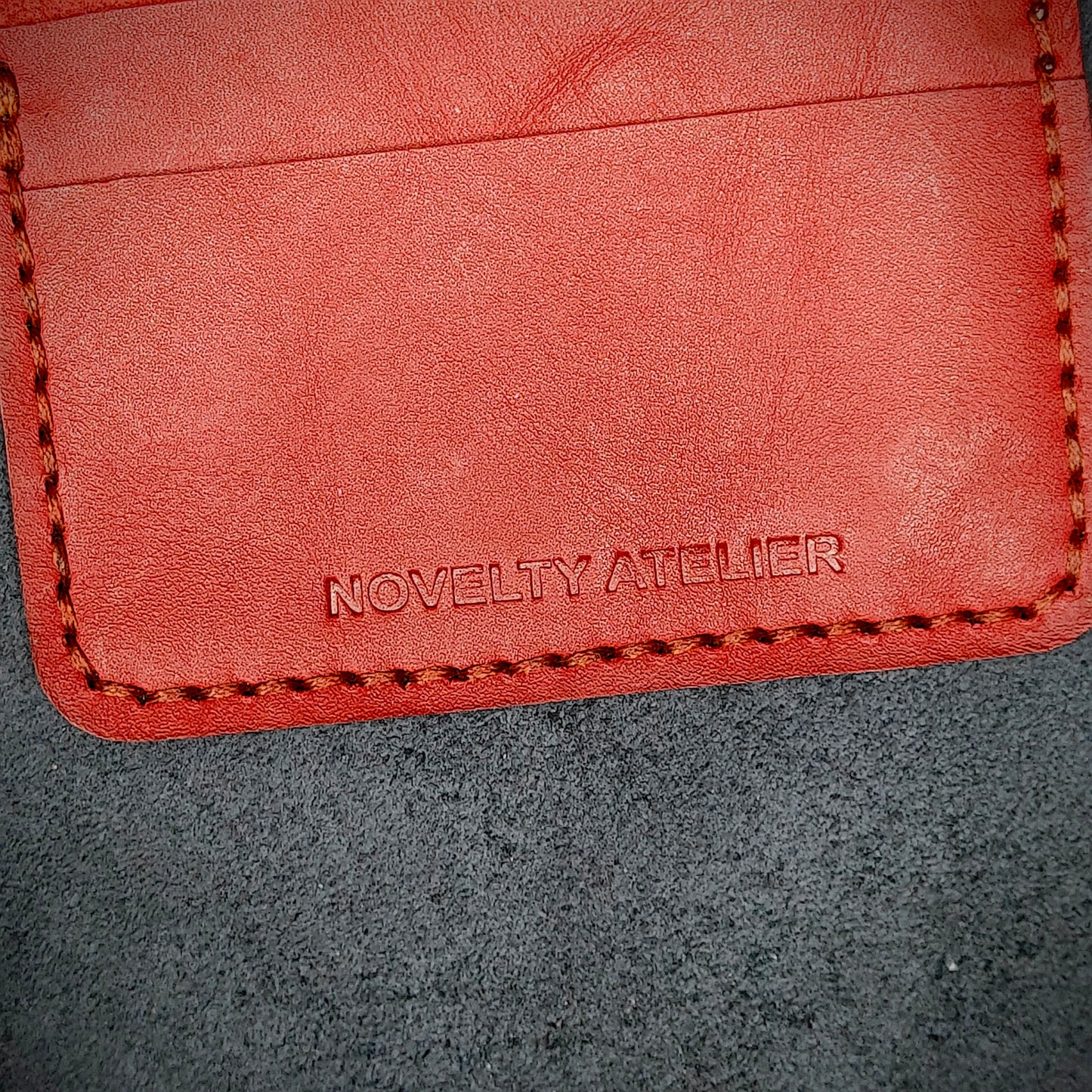 Close up of The Copperfield bifold card holder by Novelty Atelier detailed view of brand name logo embossed into Red full grain leather. Features precise saddle stitching in Red thread and hand finished edges. Symbol of artisanal craftsmanship and functional luxury.