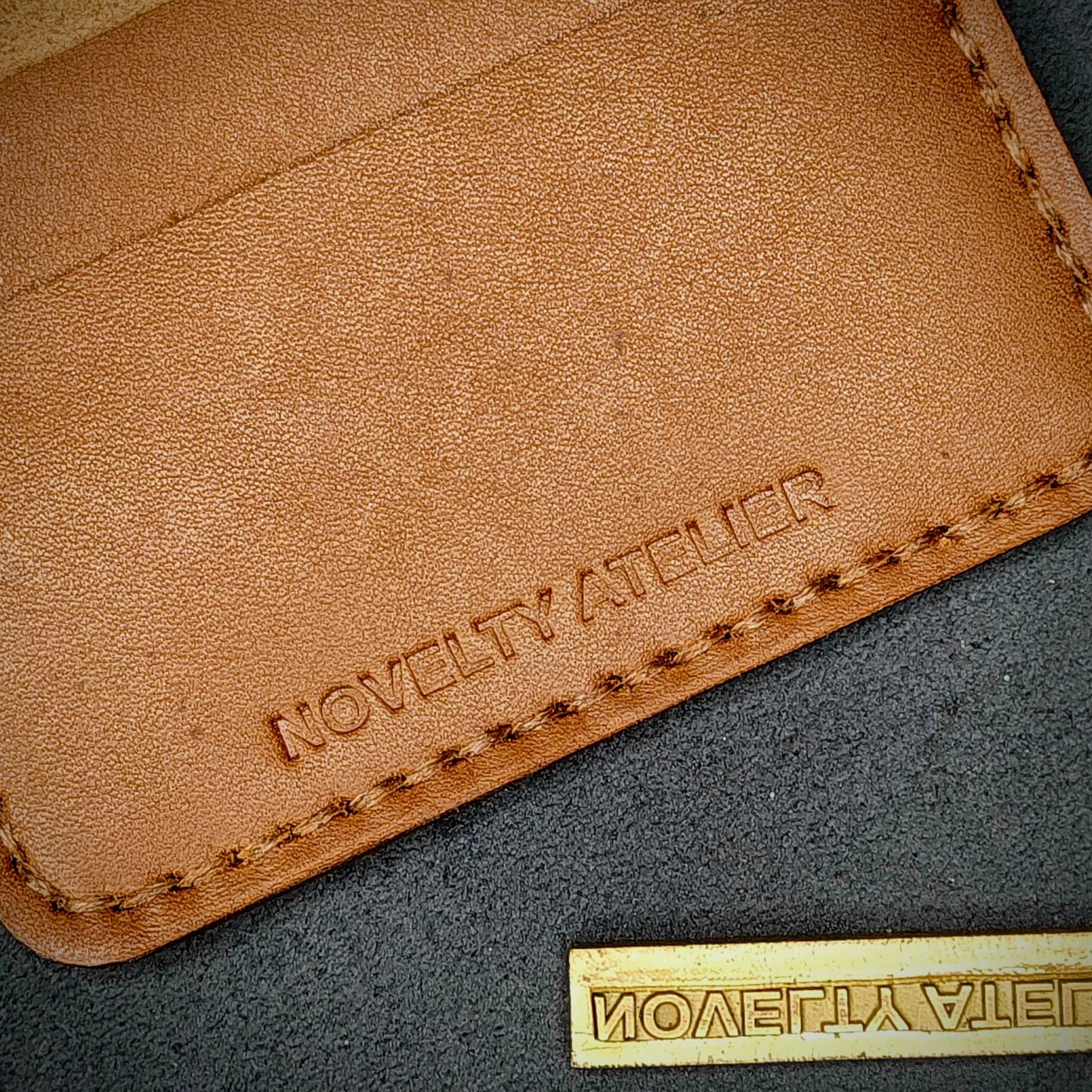 Close up of The Copperfield bifold card holder by Novelty Atelier detailed view of brand name logo embossed into Tann full grain leather. Features precise saddle stitching in Brown thread and hand finished edges. Symbol of artisanal craftsmanship and functional luxury.