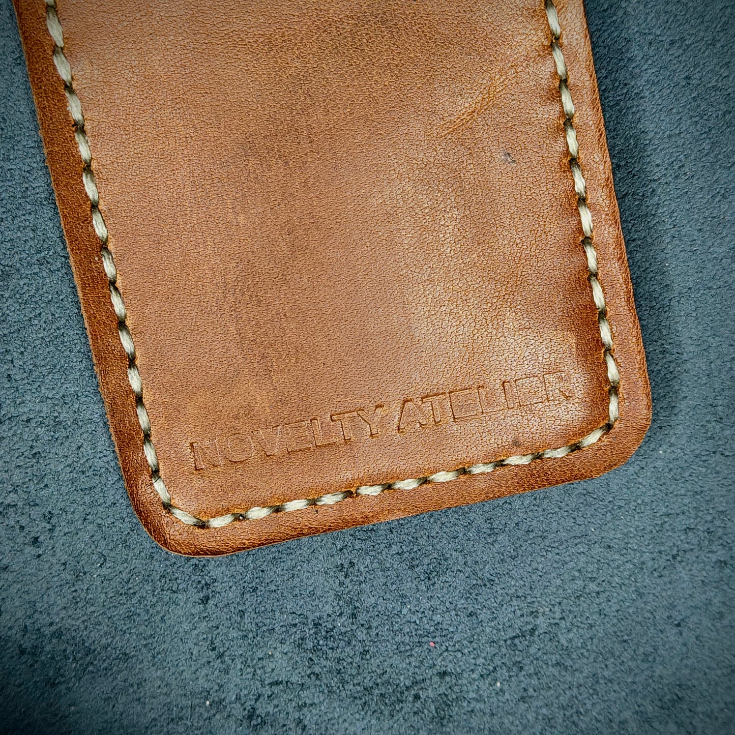 Front view close up shot of the Novelty Atelier brand emboss on The Houdini card holder – detailed close-up of premium Black and Brown full-grain leather and contrast off-white hand-stitching . Emphasizes the sharp, elegant logo impression and tactile texture, appealing to luxury EDC and minimalist gear collectors.