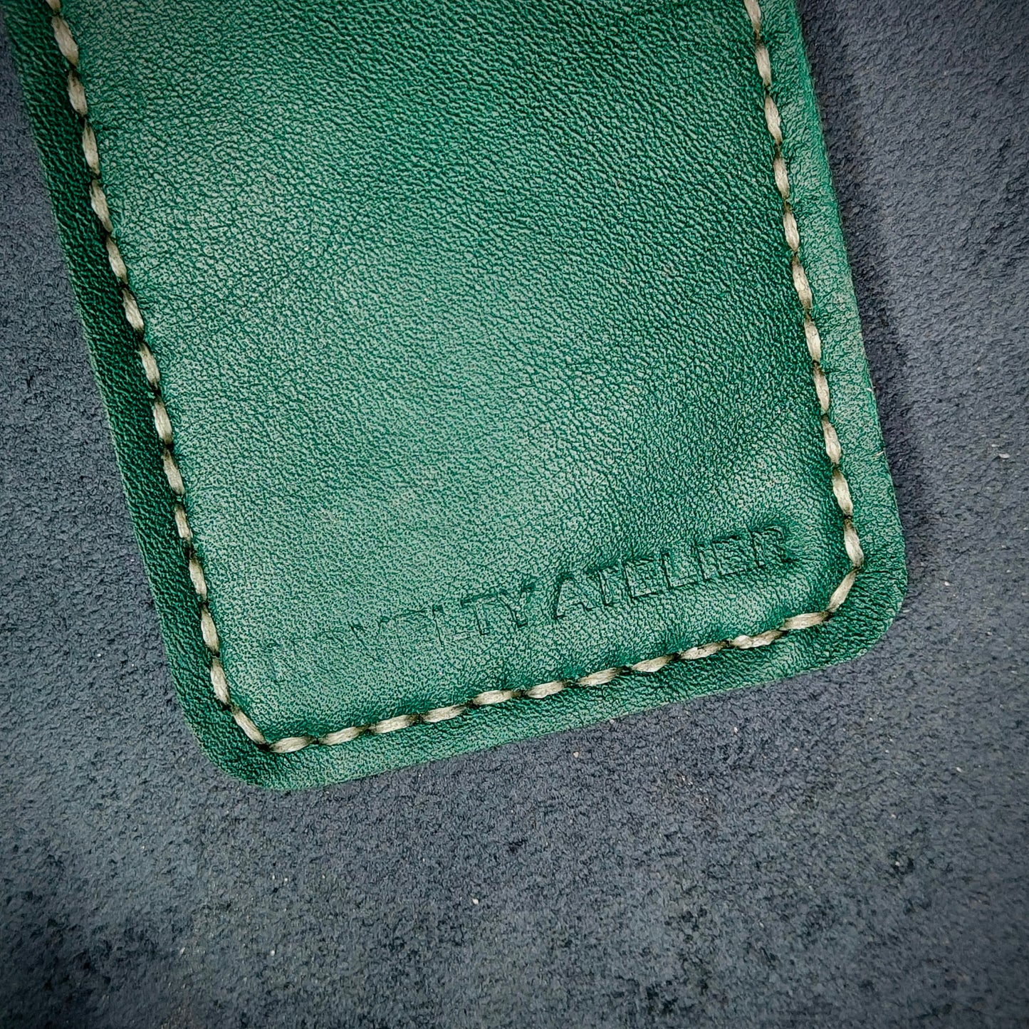 Front view close up shot of the Novelty Atelier brand emboss on The Houdini card holder – detailed close-up of premium black and green full-grain leather and contrast off white hand-stitching . Emphasizes the sharp, elegant logo impression and tactile texture, appealing to luxury EDC and minimalist gear collectors.