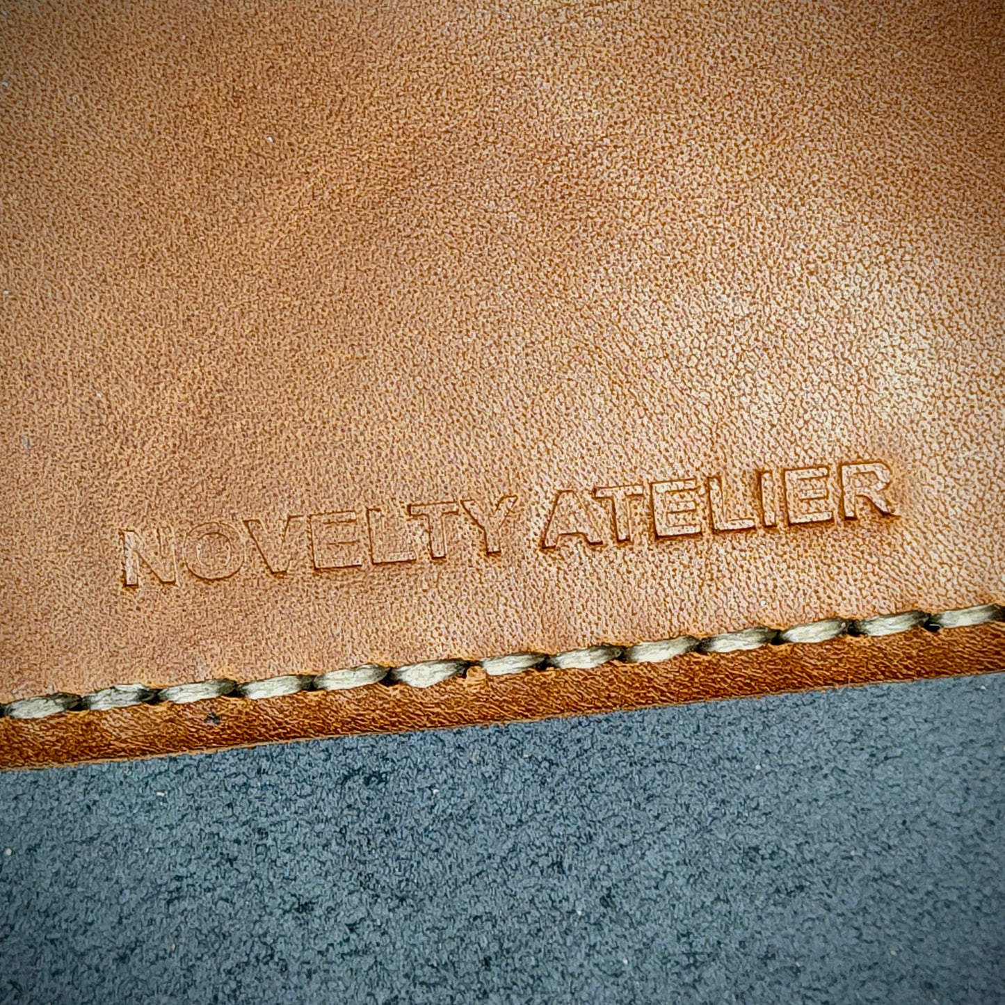 Front view close up shot of the Novelty Atelier brand emboss on The Houdini card holder horizontal configuration– detailed close-up of premium Black and Brown full-grain leather and contrast off-white hand-stitching . Emphasizes the sharp, elegant logo impression and tactile texture, appealing to luxury EDC and minimalist gear collectors.