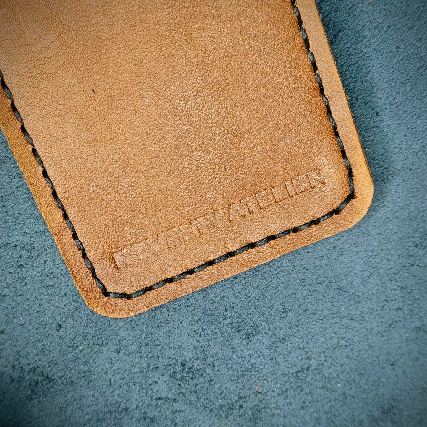 Front view close up shot of the Novelty Atelier brand emboss on The Houdini card holder in vertical configuration– detailed close-up of premium Black and Tann full-grain leather and contrast Black hand-stitching . Emphasizes the sharp, elegant logo impression and tactile texture, appealing to luxury EDC and minimalist gear collectors.