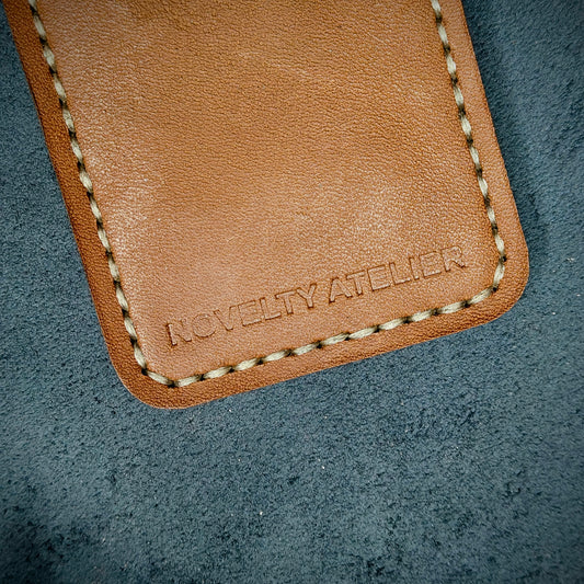 Front view close up shot of the Novelty Atelier brand emboss on The Houdini card holder in vertical configuration– detailed close-up of premium Black and Tann full-grain leather and contrast off-white hand-stitching . Emphasizes the sharp, elegant logo impression and tactile texture, appealing to luxury EDC and minimalist gear collectors.