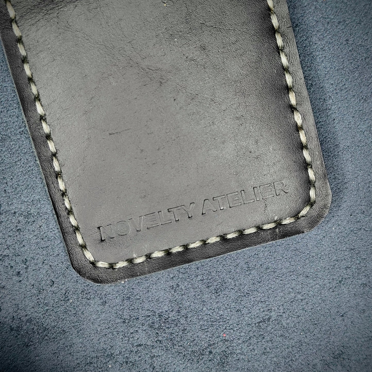 Front view close up shot of the Novelty Atelier brand emboss on The Houdini card holder in vertical configuration– detailed close-up of premium Black full-grain leather and contrast off-white hand-stitching . Emphasizes the sharp, elegant logo impression and tactile texture, appealing to luxury EDC and minimalist gear collectors.