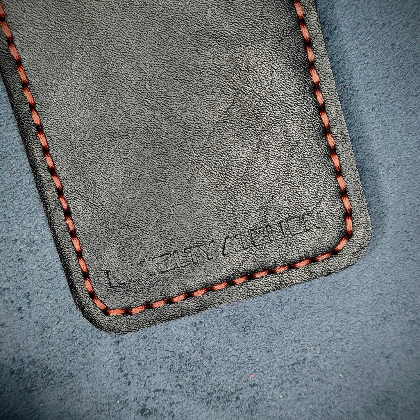 Front view close up shot of the Novelty Atelier brand emboss on The Houdini card holder in vertical configuration– detailed close-up of premium Black full-grain leather and contrast red hand-stitching . Emphasizes the sharp, elegant logo impression and tactile texture, appealing to luxury EDC and minimalist gear collectors.