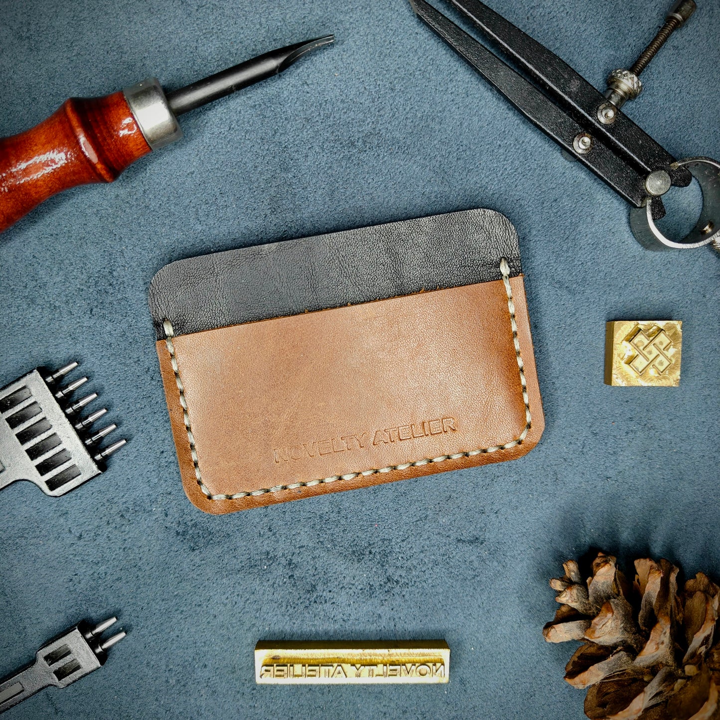Front view of The Houdini minimalist card holder in horizontal configuration by Novelty Atelier – handcrafted from Black and Brown ethically sourced full-grain leather with contrasting off-white saddle stitching. Features the “Novelty Atelier” brand name cleanly embossed on the front. Perfectly balanced minimalist wallet design tailored for modern EDC enthusiasts who value craftsmanship and brand integrity.