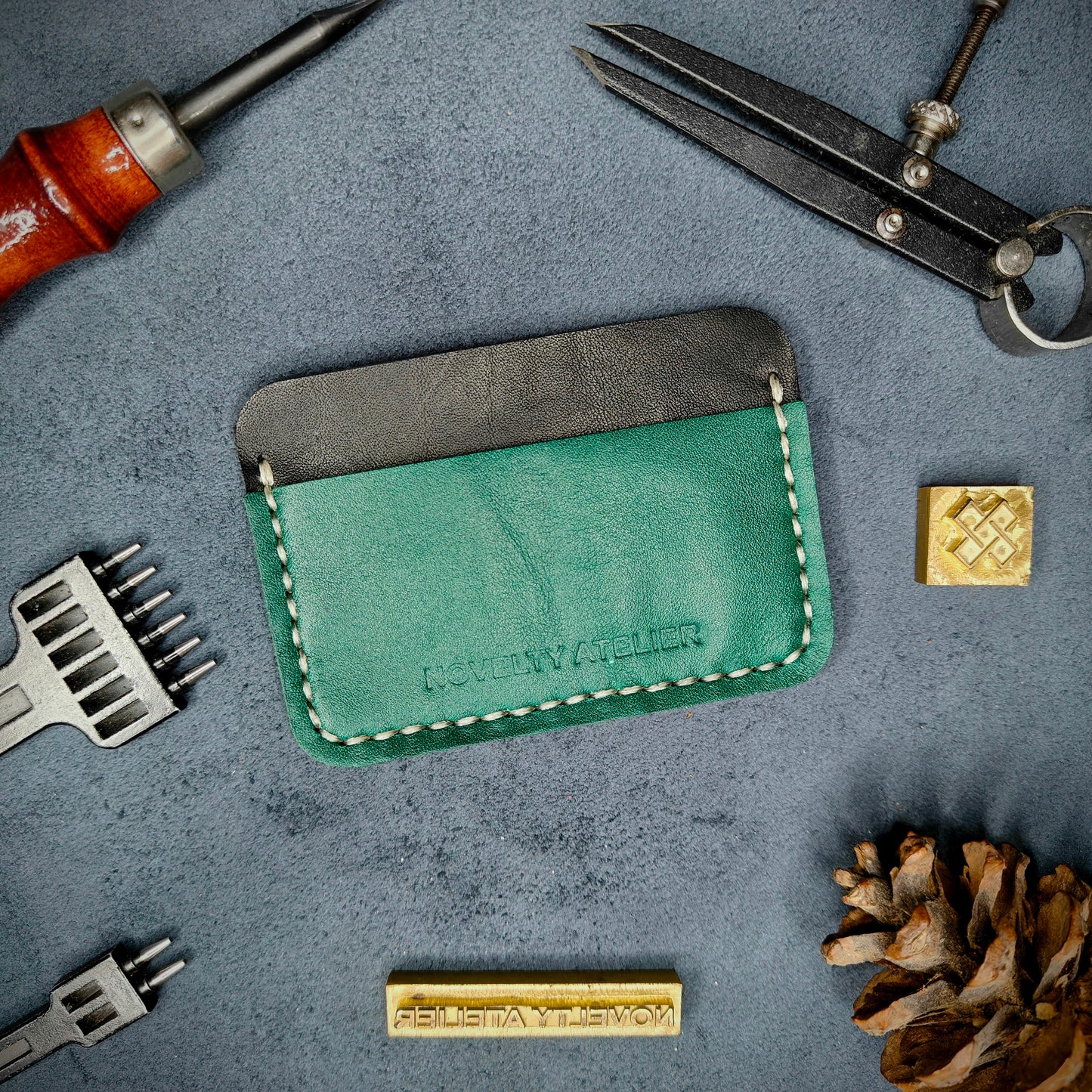 Front view of The Houdini minimalist card holder in horizontal configuration by Novelty Atelier – handcrafted from black and green ethically sourced full-grain leather with contrasting off white saddle stitching. Features the “Novelty Atelier” brand name cleanly embossed on the front. Perfectly balanced minimalist wallet design tailored for modern EDC enthusiasts who value craftsmanship and brand integrity.