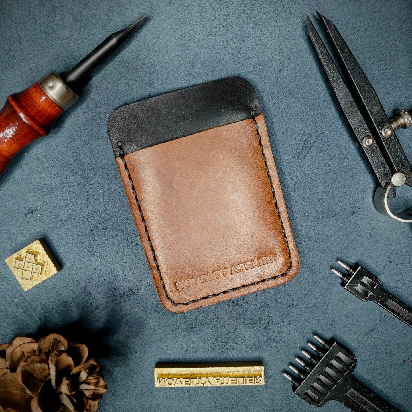 Front view of The Houdini minimalist card holder in vertical configuration by Novelty Atelier – handcrafted from Black and Brown ethically sourced full-grain leather with contrasting Black saddle stitching. Features the “Novelty Atelier” brand name cleanly embossed on the front. Perfectly balanced minimalist wallet design tailored for modern EDC enthusiasts who value craftsmanship and brand integrity.