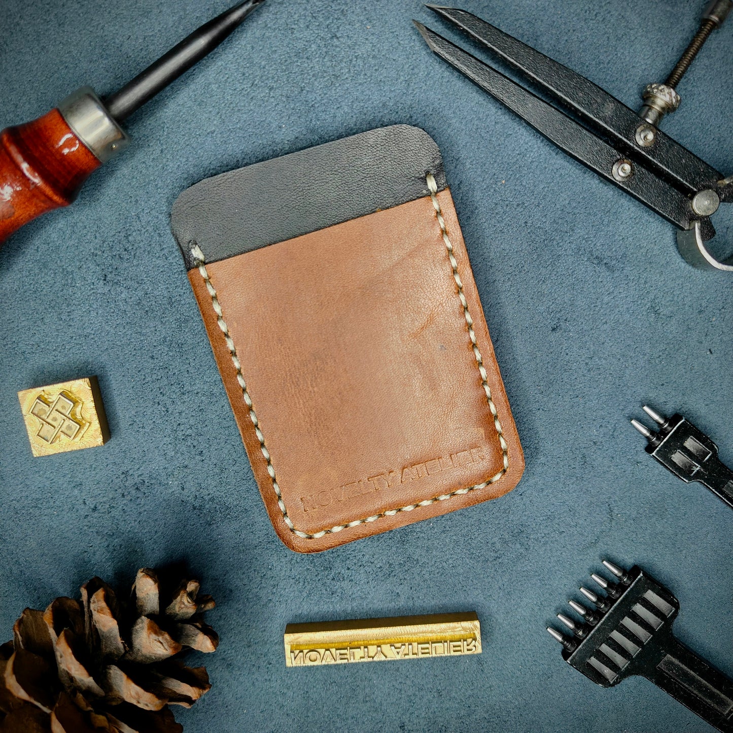 Front view of The Houdini minimalist card holder in vertical configuration by Novelty Atelier – handcrafted from Black and Brown ethically sourced full-grain leather with contrasting off-white saddle stitching. Features the “Novelty Atelier” brand name cleanly embossed on the front. Perfectly balanced minimalist wallet design tailored for modern EDC enthusiasts who value craftsmanship and brand integrity.