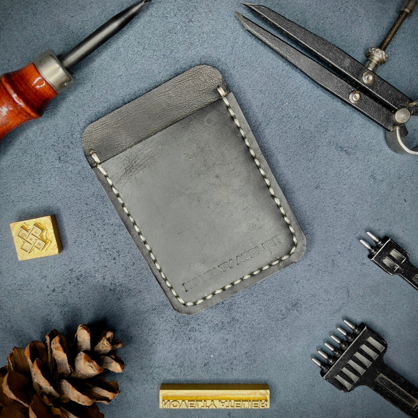 Front view of The Houdini minimalist card holder in vertical configuration by Novelty Atelier – handcrafted from Black ethically sourced full-grain leather with contrasting off-white saddle stitching. Features the “Novelty Atelier” brand name cleanly embossed on the front. Perfectly balanced minimalist wallet design tailored for modern EDC enthusiasts who value craftsmanship and brand integrity.