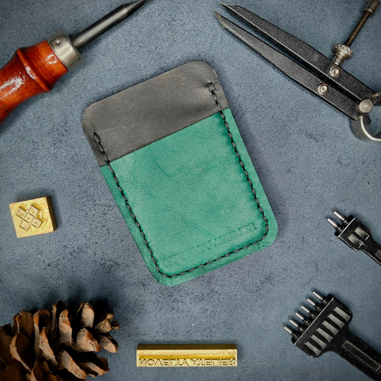 Front view of The Houdini minimalist card holder in vertical configuration by Novelty Atelier – handcrafted from black and green ethically sourced full-grain leather with contrasting black saddle stitching. Features the “Novelty Atelier” brand name cleanly embossed on the front. Perfectly balanced minimalist wallet design tailored for modern EDC enthusiasts who value craftsmanship and brand integrity.