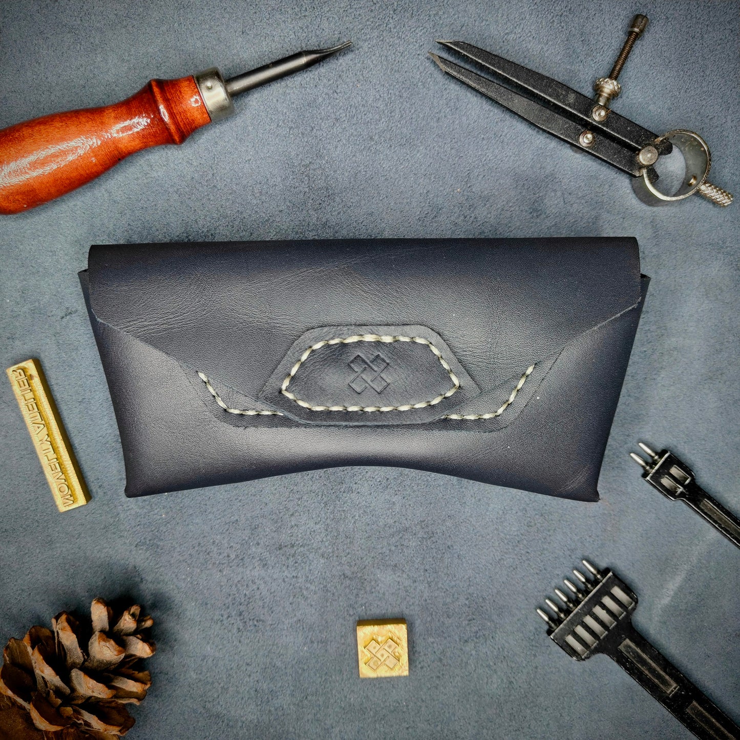 The Hustler - Sunglass case Navy blue full grain leather - closed with magnetic snap Detailed picture showing the logo with tools surrounding for aesthetics