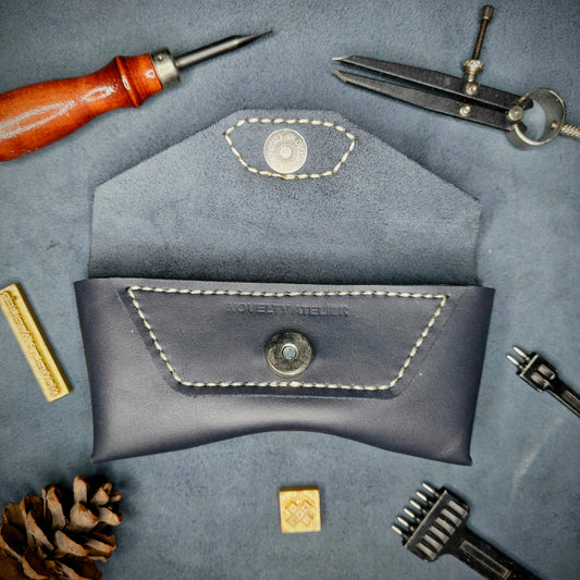 The Hustler - Sunglass case Navy blue full grain leather - open with magnetic snap detailed picture showing the brand name logo with tools surrounding for aesthetics