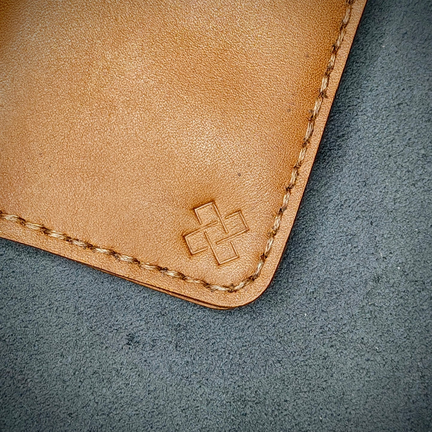 Zoomed in view of Novelty Atelier’s signature insignia embossed on The Copperfield minimalist leather card holder. Hand stitched in Brown thread using traditional saddle technique. Crafted from Tann full grain leather, symbolizing timeless durability and ethical sophistication.