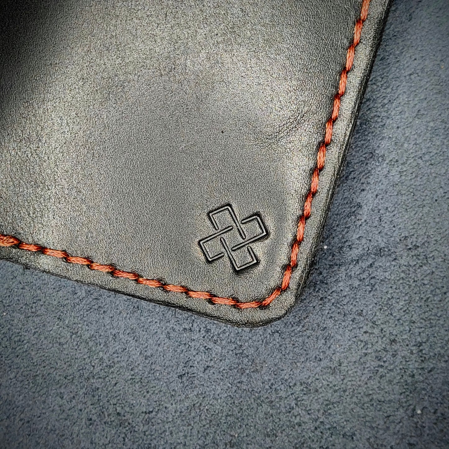 Zoomed in view of Novelty Atelier’s signature insignia embossed on The Copperfield minimalist leather card holder. Hand stitched in Red thread using traditional saddle technique. Crafted from Black full grain leather, symbolizing timeless durability and ethical sophistication.
