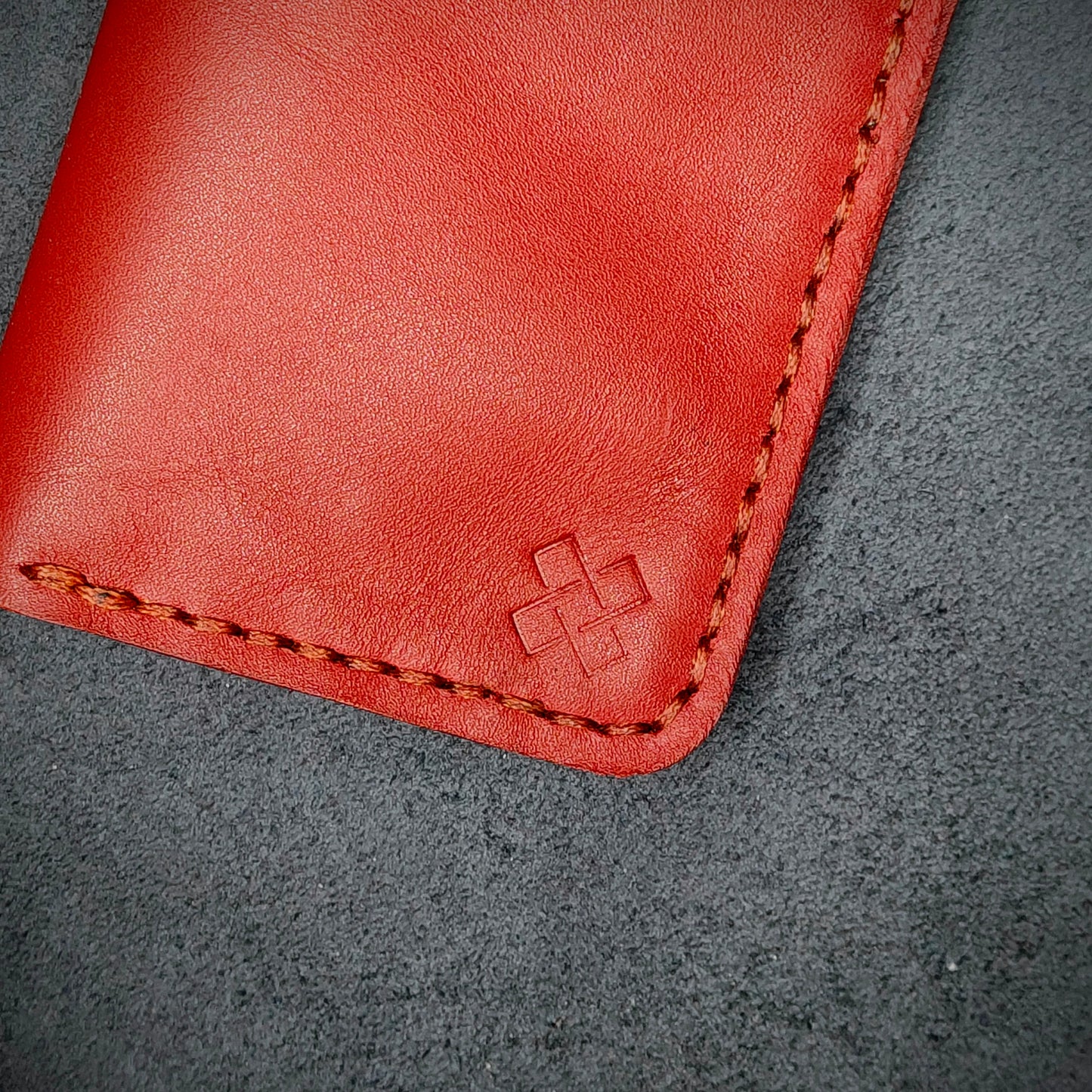 Zoomed in view of Novelty Atelier’s signature insignia embossed on The Copperfield minimalist leather card holder. Hand stitched in Red thread using traditional saddle technique. Crafted from Red full grain leather, symbolizing timeless durability and ethical sophistication.
