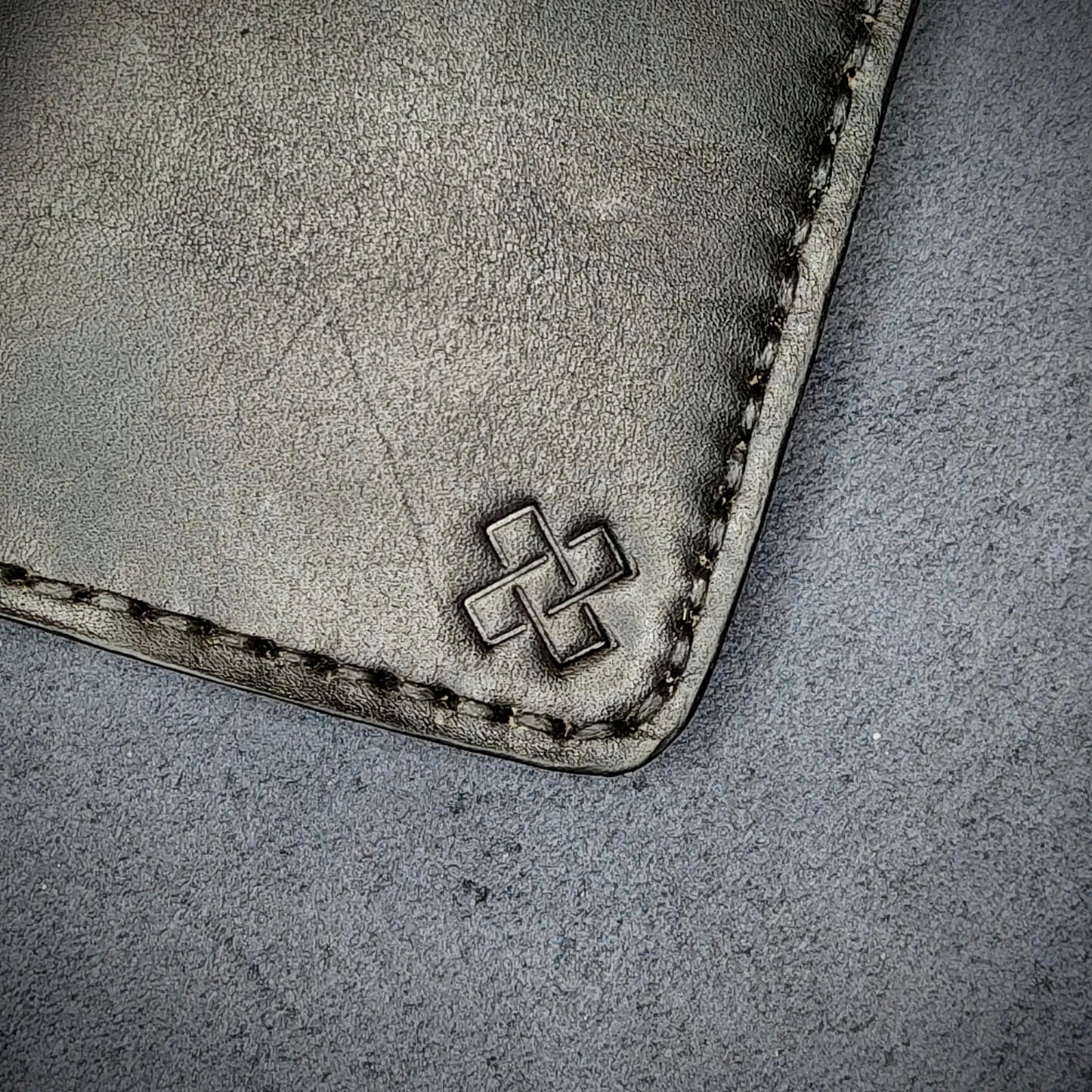 Zoomed in view of Novelty Atelier’s signature insignia embossed on The Copperfield minimalist leather card holder. Hand stitched in black thread using traditional saddle technique. Crafted from Black full grain leather, symbolizing timeless durability and ethical sophistication.