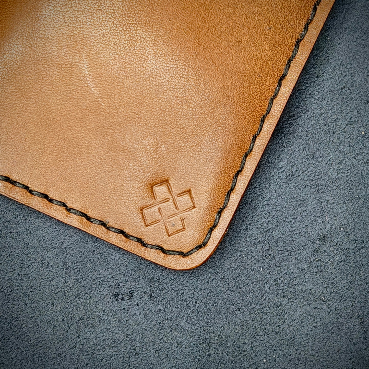 Zoomed in view of Novelty Atelier’s signature insignia embossed on The Copperfield minimalist leather card holder. Hand stitched in black thread using traditional saddle technique. Crafted from Tann full grain leather, symbolizing timeless durability and ethical sophistication.