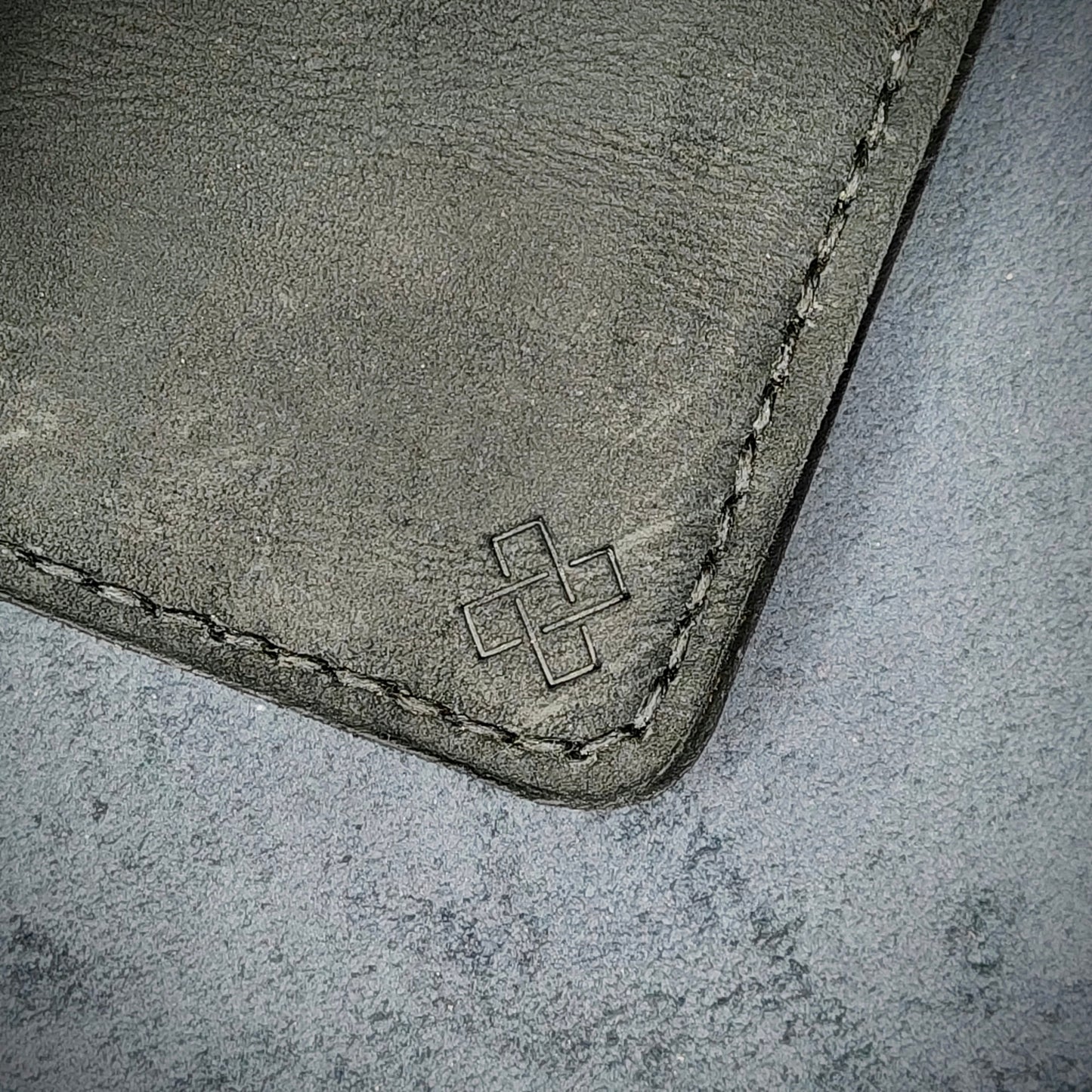 Zoomed in view of Novelty Atelier’s signature insignia embossed on The Copperfield minimalist leather card holder. Hand stitched in black thread using traditional saddle technique. Crafted from full grain Black and Brown leather, symbolizing timeless durability and ethical sophistication.