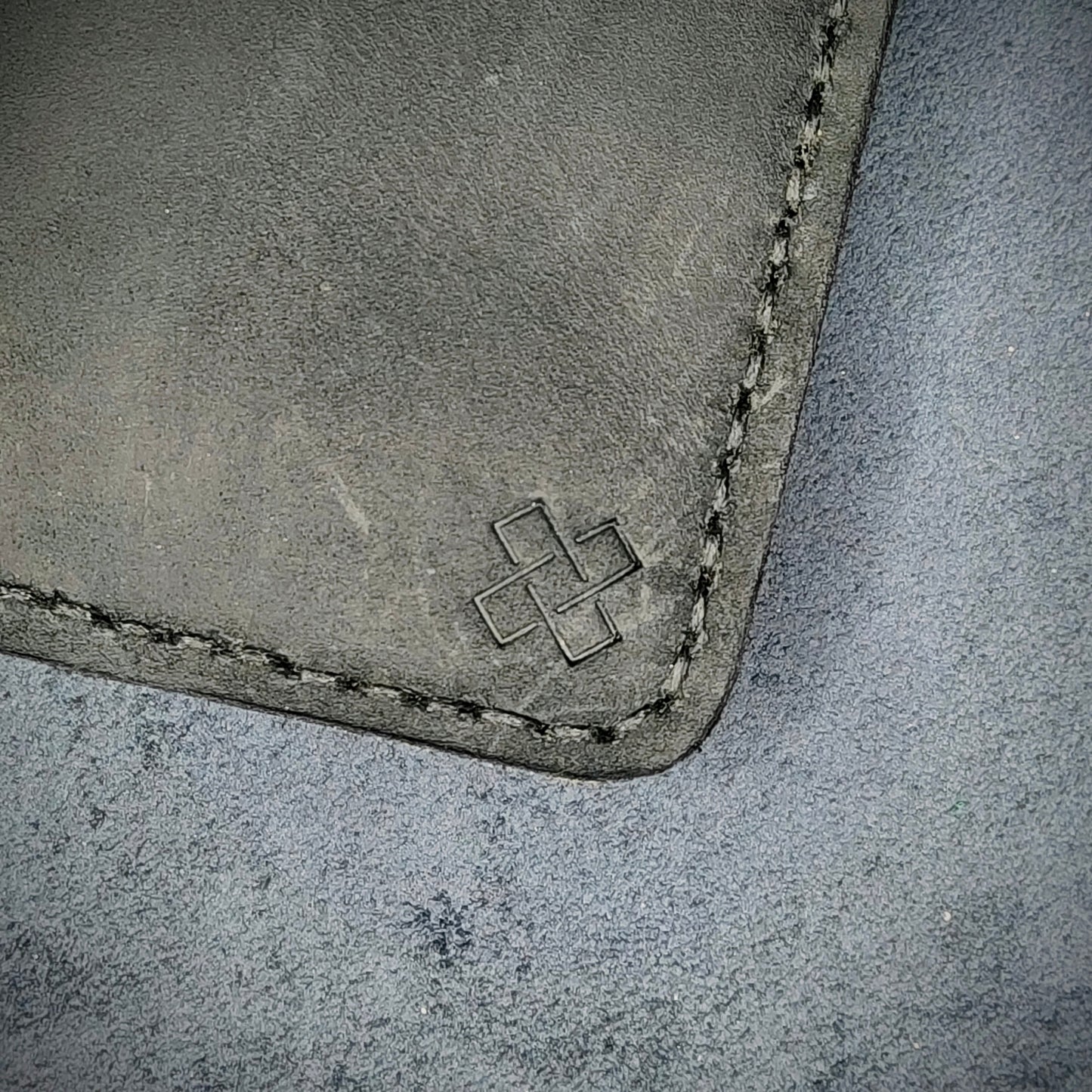 Zoomed in view of Novelty Atelier’s signature insignia embossed on The Copperfield minimalist leather card holder. Hand stitched in black thread using traditional saddle technique. Crafted from full grain Black and Mustard yellow leather, symbolizing timeless durability and ethical sophistication.