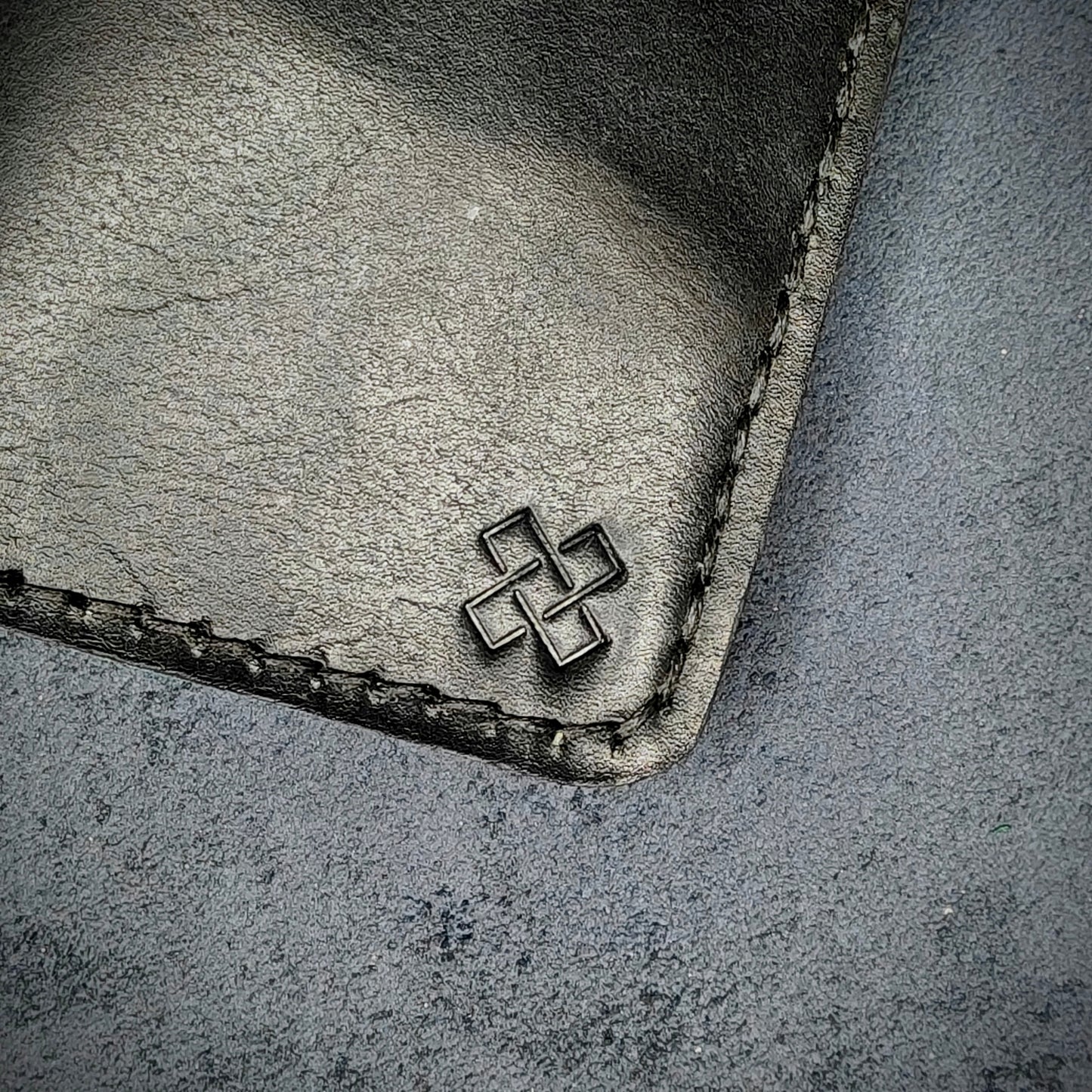 Zoomed in view of Novelty Atelier’s signature insignia embossed on The Copperfield minimalist leather card holder. Hand stitched in black thread using traditional saddle technique. Crafted from full grain Black and Green leather, symbolizing timeless durability and ethical sophistication.