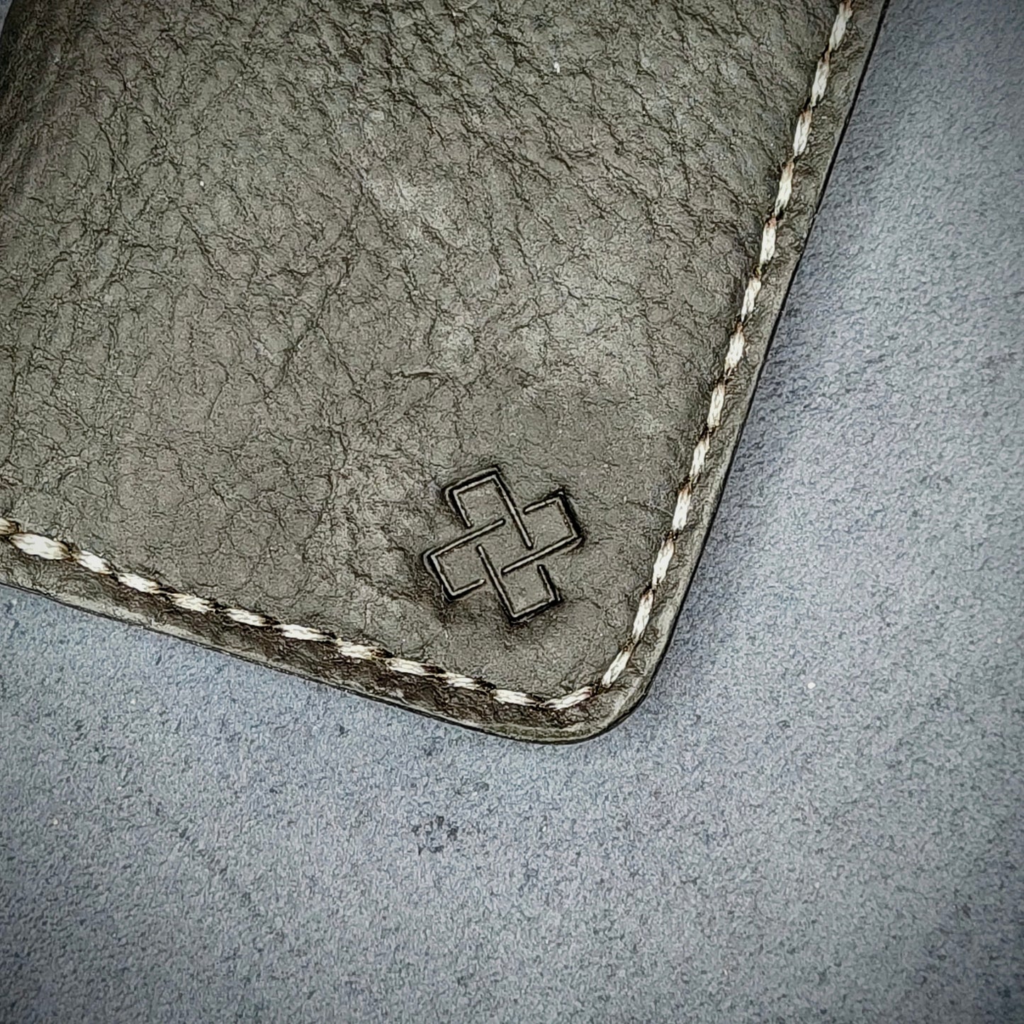 Zoomed in view of Novelty Atelier’s signature insignia embossed on The Copperfield minimalist leather card holder. Hand stitched in off white thread using traditional saddle technique. Crafted from Black full grain leather, symbolizing timeless durability and ethical sophistication.