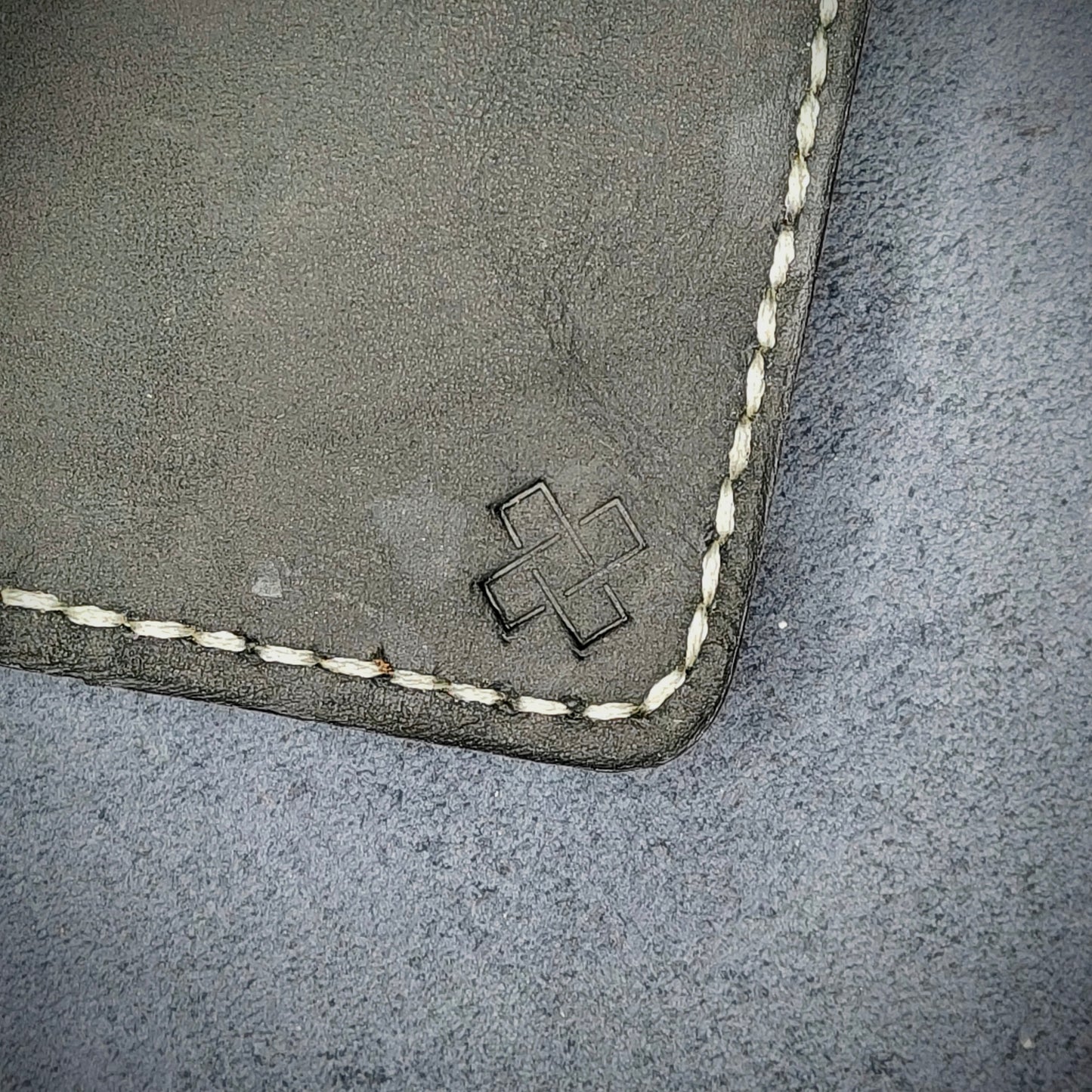Zoomed in view of Novelty Atelier’s signature insignia embossed on The Copperfield minimalist leather card holder. Hand stitched in off white thread using traditional saddle technique. Crafted from full grain Black and Brown leather, symbolizing timeless durability and ethical sophistication.