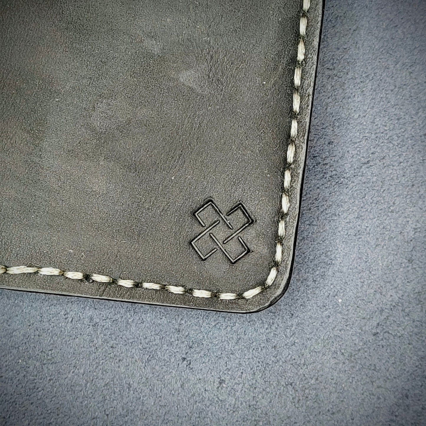 Zoomed in view of Novelty Atelier’s signature insignia embossed on The Copperfield minimalist leather card holder. Hand stitched in off white thread using traditional saddle technique. Crafted from full grain Black and Mustard yellow leather, symbolizing timeless durability and ethical sophistication.