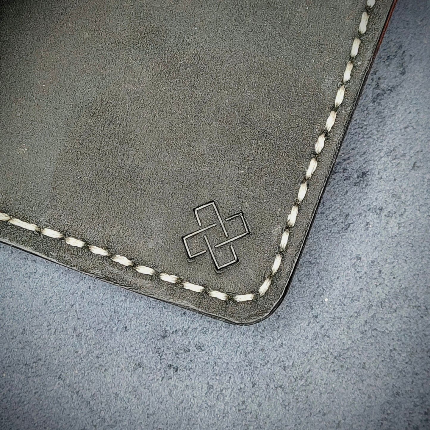 Zoomed in view of Novelty Atelier’s signature insignia embossed on The Copperfield minimalist leather card holder. Hand stitched in off white thread using traditional saddle technique. Crafted from full grain Black and Purple leather, symbolizing timeless durability and ethical sophistication.