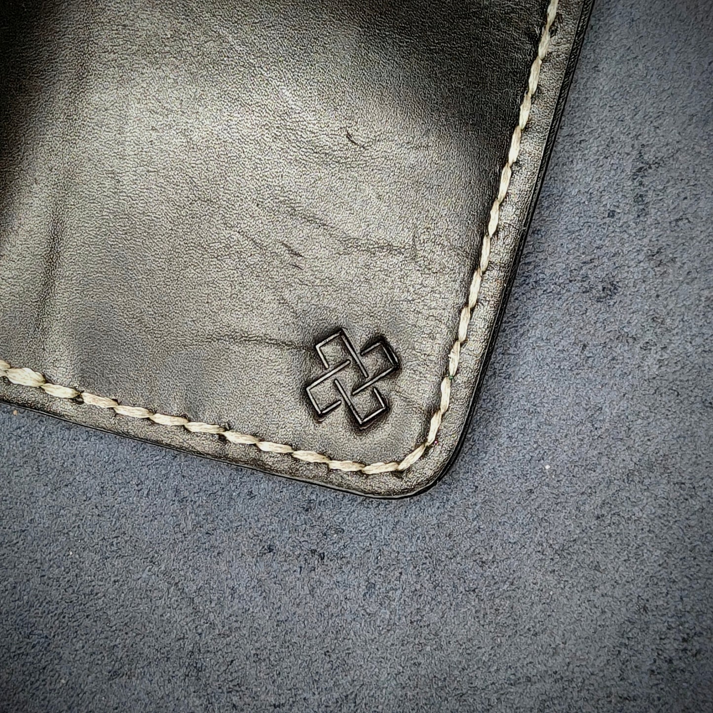 Zoomed in view of Novelty Atelier’s signature insignia embossed on The Copperfield minimalist leather card holder. Hand stitched in off white thread using traditional saddle technique. Crafted from full grain Black and Green leather, symbolizing timeless durability and ethical sophistication.