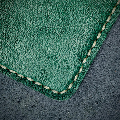 Back view close-up of the design logo emboss on the back of The Houdini card holder– focusing on the fine grain detail of ethically sourced green full-grain leather and meticulous off-white saddle stitching. Showcases the subtle artistry and understated luxury of Novelty Atelier’s craftsmanship.
