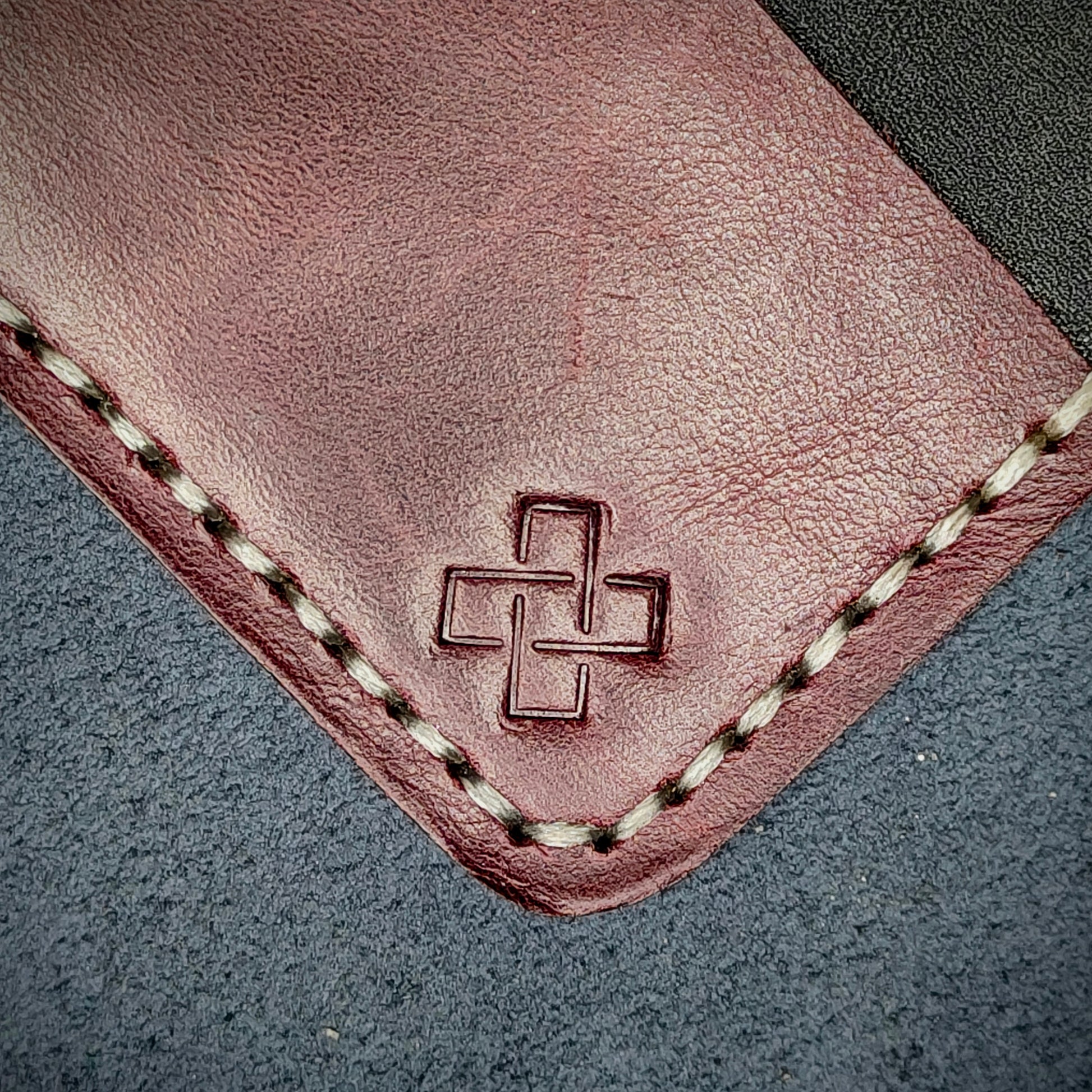 Back view close-up of the design logo emboss on the back of The Houdini card holder in horizontal configuration– focusing on the fine grain detail of ethically sourced Purple full-grain leather and meticulous off-white saddle stitching. Showcases the subtle artistry and understated luxury of Novelty Atelier’s craftsmanship.
